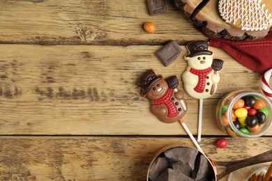 Photo of Flat lay composition with funny chocolate snowmen candies on wooden table. Space for text