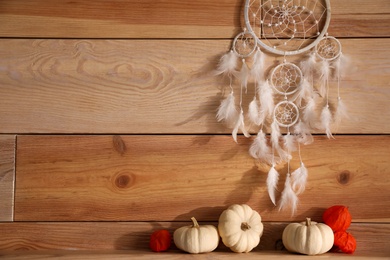 Beautiful dream catcher, white pumpkins and calyces of physalis near wooden wall, space for text