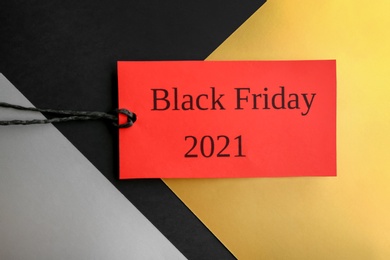 Photo of Red tag with words BLACK FRIDAY 2021 on color background, top view