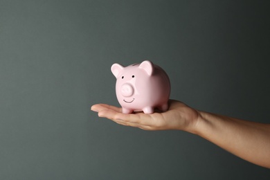 Photo of Woman holding piggy bank on dark grey background, closeup view
