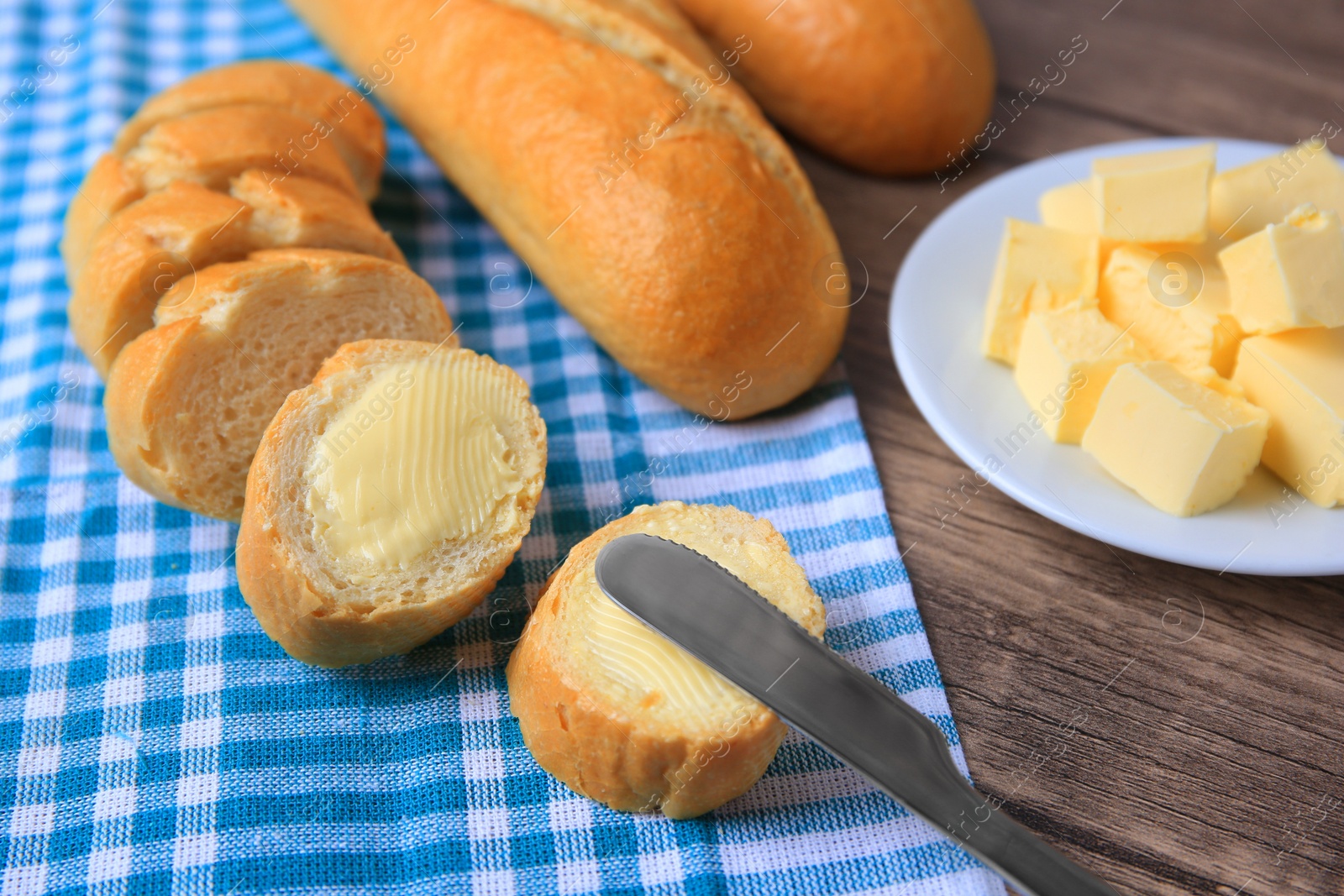 Photo of Tasty cut baguette with fresh butter on wooden table, closeup