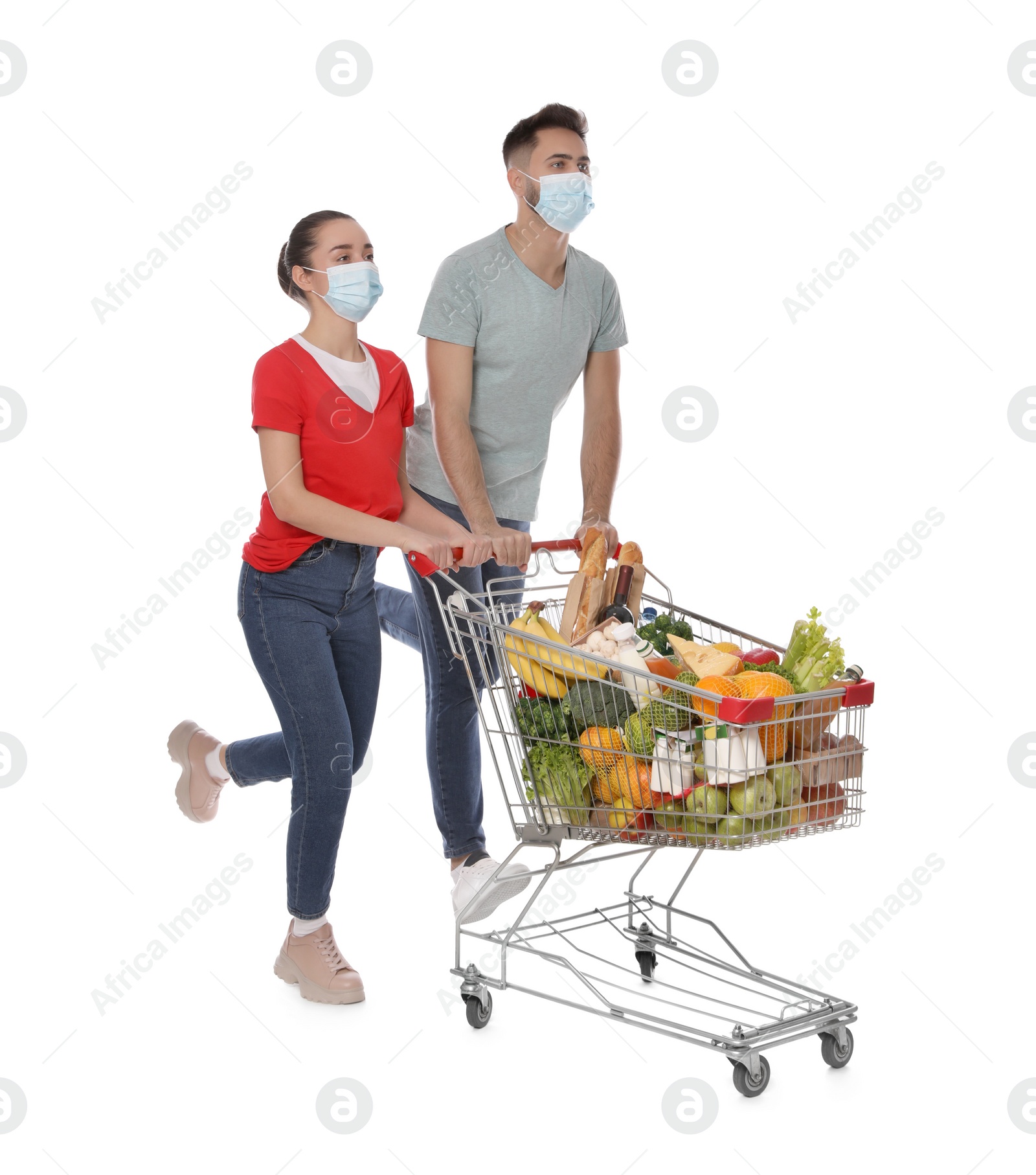 Photo of Couple with protective masks and shopping cart full of groceries on white background