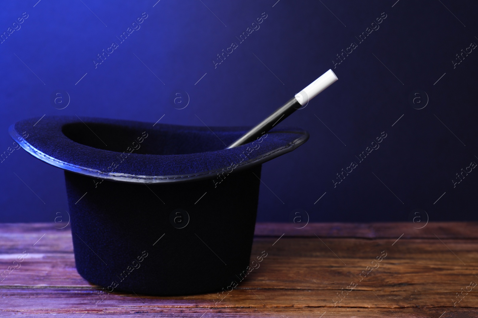 Photo of Black top hat and wand on wooden table, space for text. Magician equipment