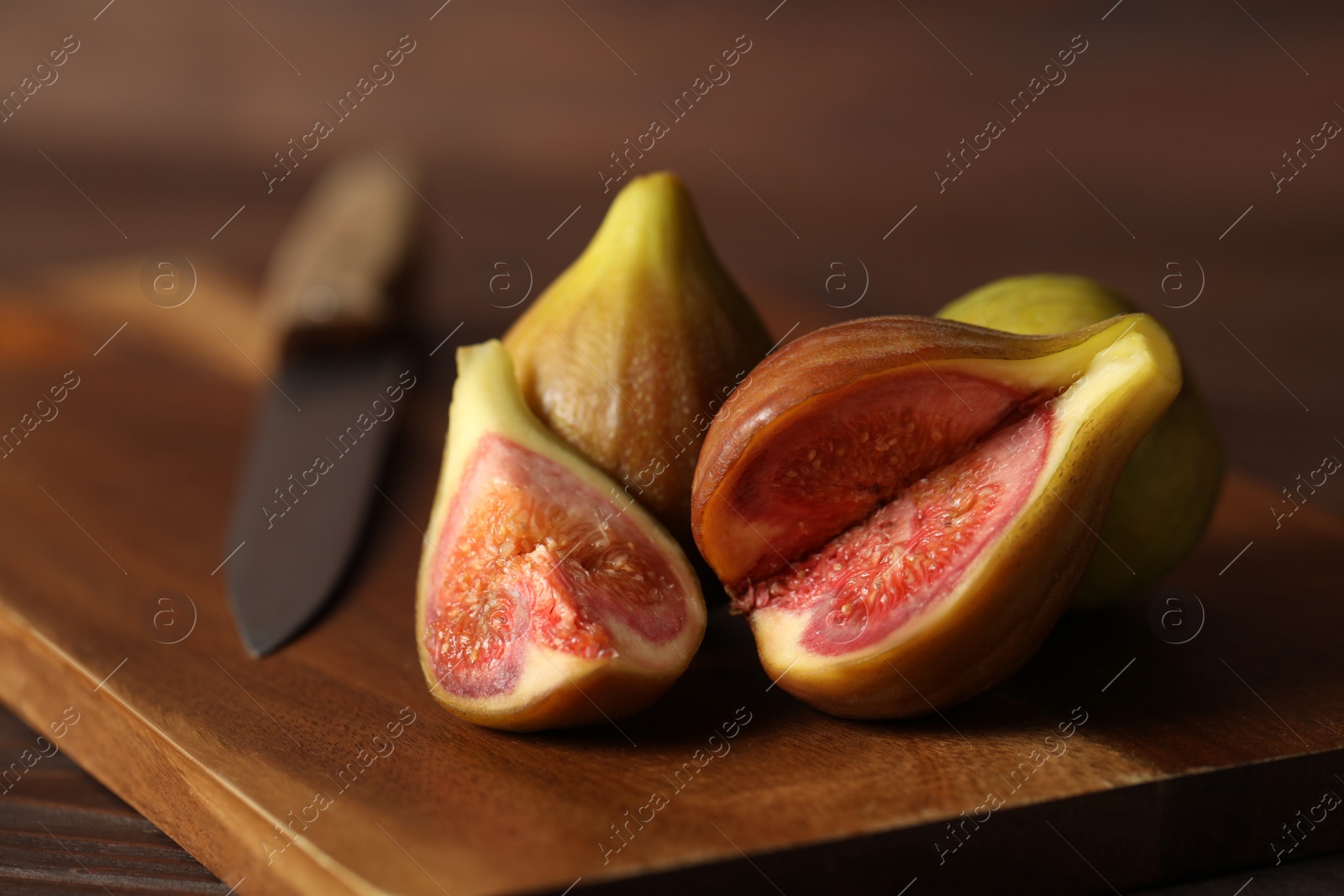 Photo of Tasty raw figs and knife on wooden board, closeup