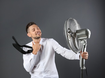 Photo of Man refreshing from heat in front of fan on grey background