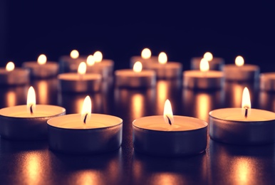 Photo of Wax candles burning on table in darkness, closeup