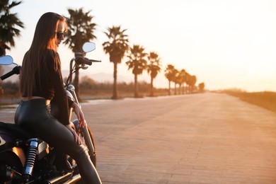 Photo of Beautiful young woman sitting on motorcycle outdoors. Space for text