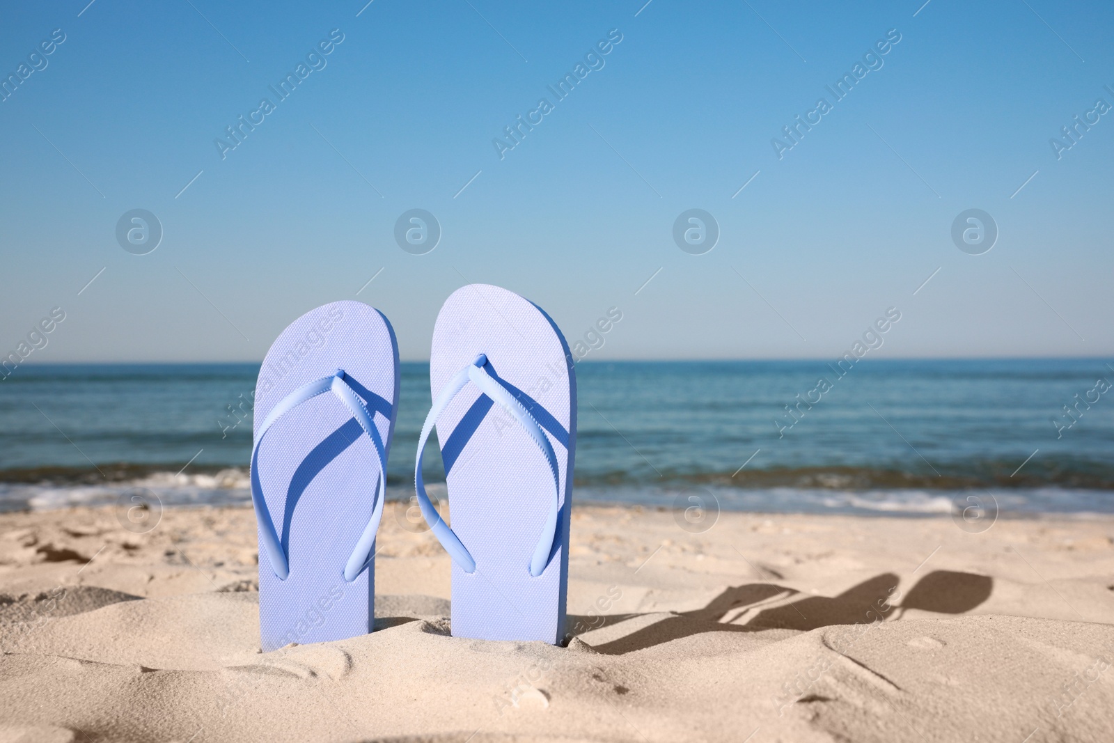 Photo of Stylish flip flops in sand on beach. Space for text