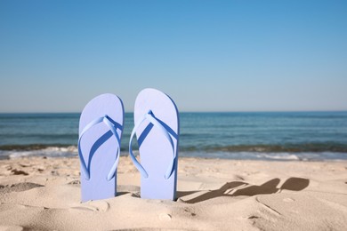 Photo of Stylish flip flops in sand on beach. Space for text