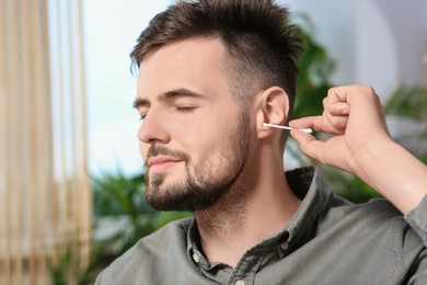 Photo of Young man cleaning ear with cotton swab at home