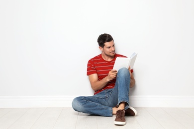 Photo of Handsome man reading book on floor near white wall