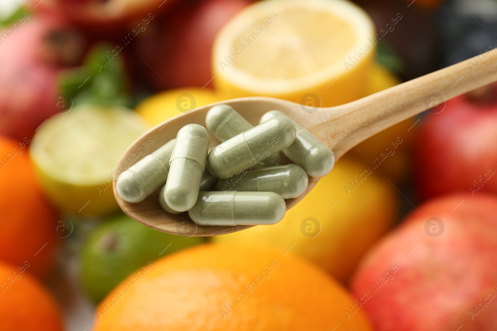 Photo of Vitamin pills in spoon against fresh fruits, closeup