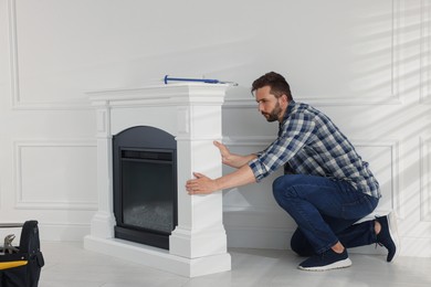 Photo of Man installing electric fireplace near white wall in room