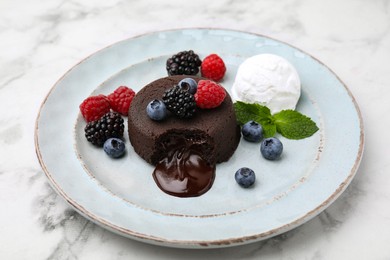 Delicious chocolate fondant served with fresh berries and ice cream on white marble table, closeup