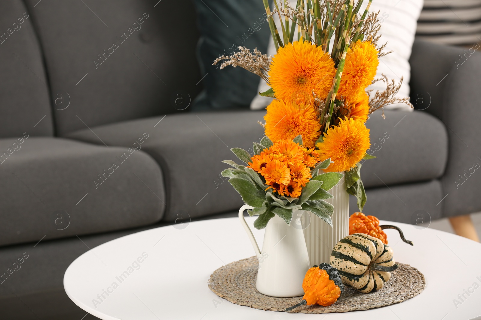 Photo of Beautiful autumn bouquets and pumpkins on coffee table near sofa in room