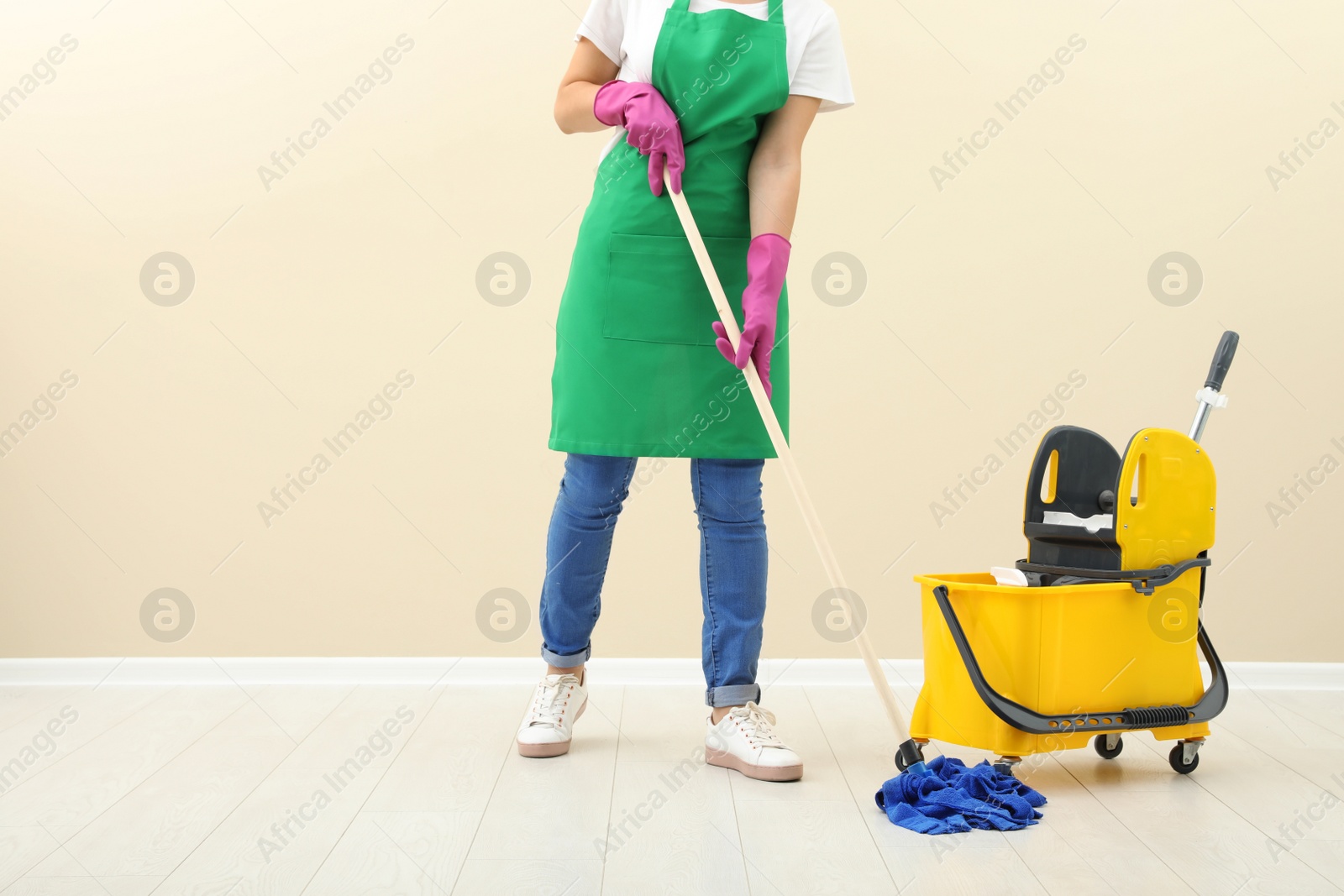 Photo of Young woman with mop cleaning floor near light wall