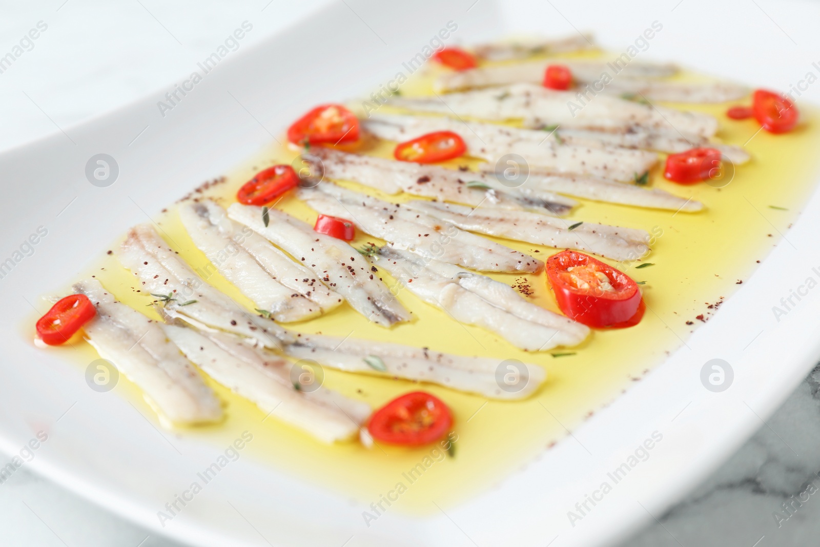 Photo of Tasty pickled anchovies with spices on plate, closeup