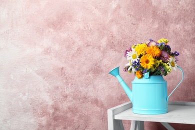 Watering can with beautiful wild flowers on table against color background