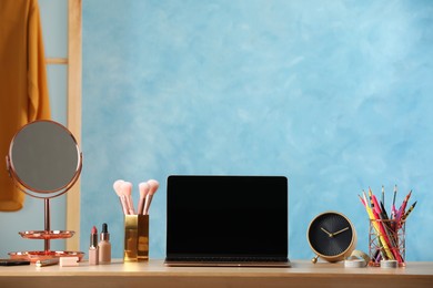 Photo of Wooden table with modern laptop and makeup products in room