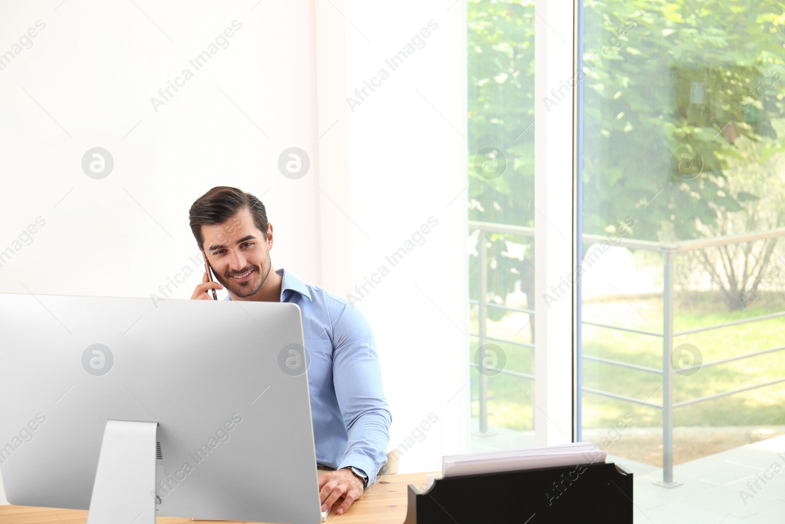 Photo of Handsome young man working with smartphone and computer at table in office