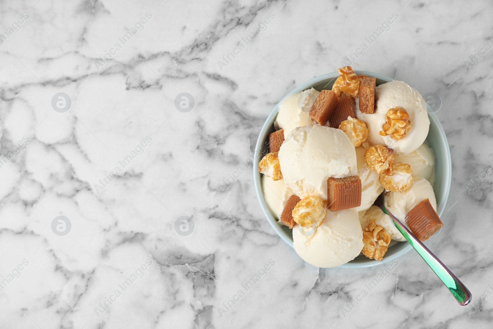 Photo of Plate of delicious ice cream with caramel candies and popcorn on white marble table, top view. Space for text