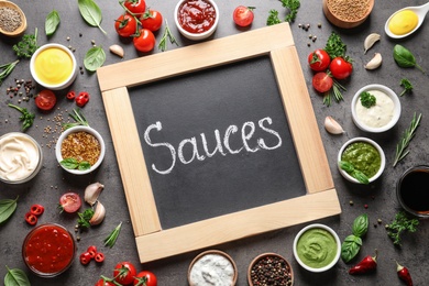 Small blackboard with word Sauces and different dressings on gray background, flat lay