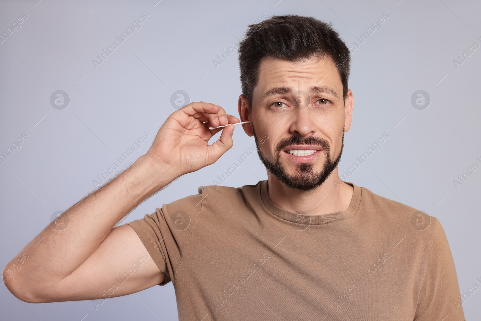 Photo of Emotional man cleaning ears on grey background