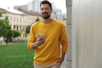 Handsome man with smartphone walking on city street