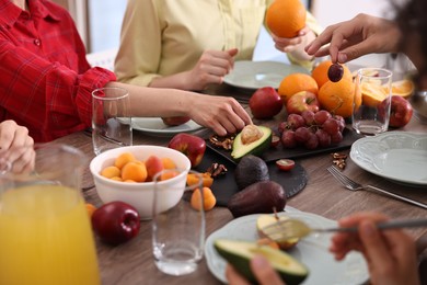 Photo of Vegetarian food. Friends eating fresh fruits at wooden table indoors, closeup