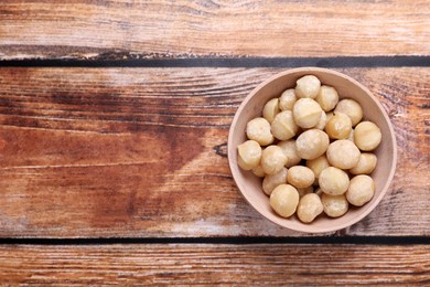 Photo of Delicious peeled Macadamia nuts in bowl on wooden table, top view. Space for text