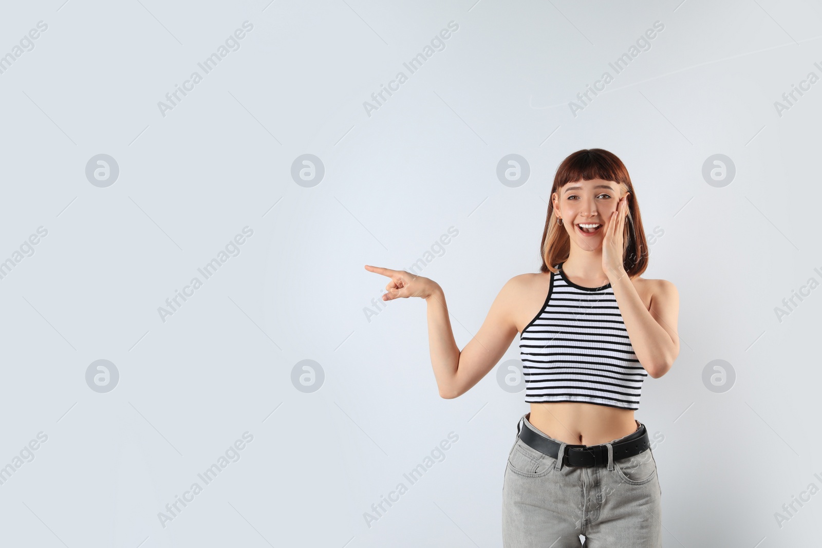 Photo of Excited girl pointing at something on white background. Space for text