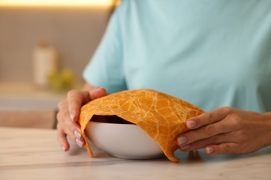 Photo of Woman packing bowl into beeswax food wrap at light table in kitchen, closeup