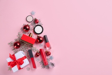 Photo of Christmas tree shape of decorative cosmetic products on pink background, flat lay with space for text. Winter care