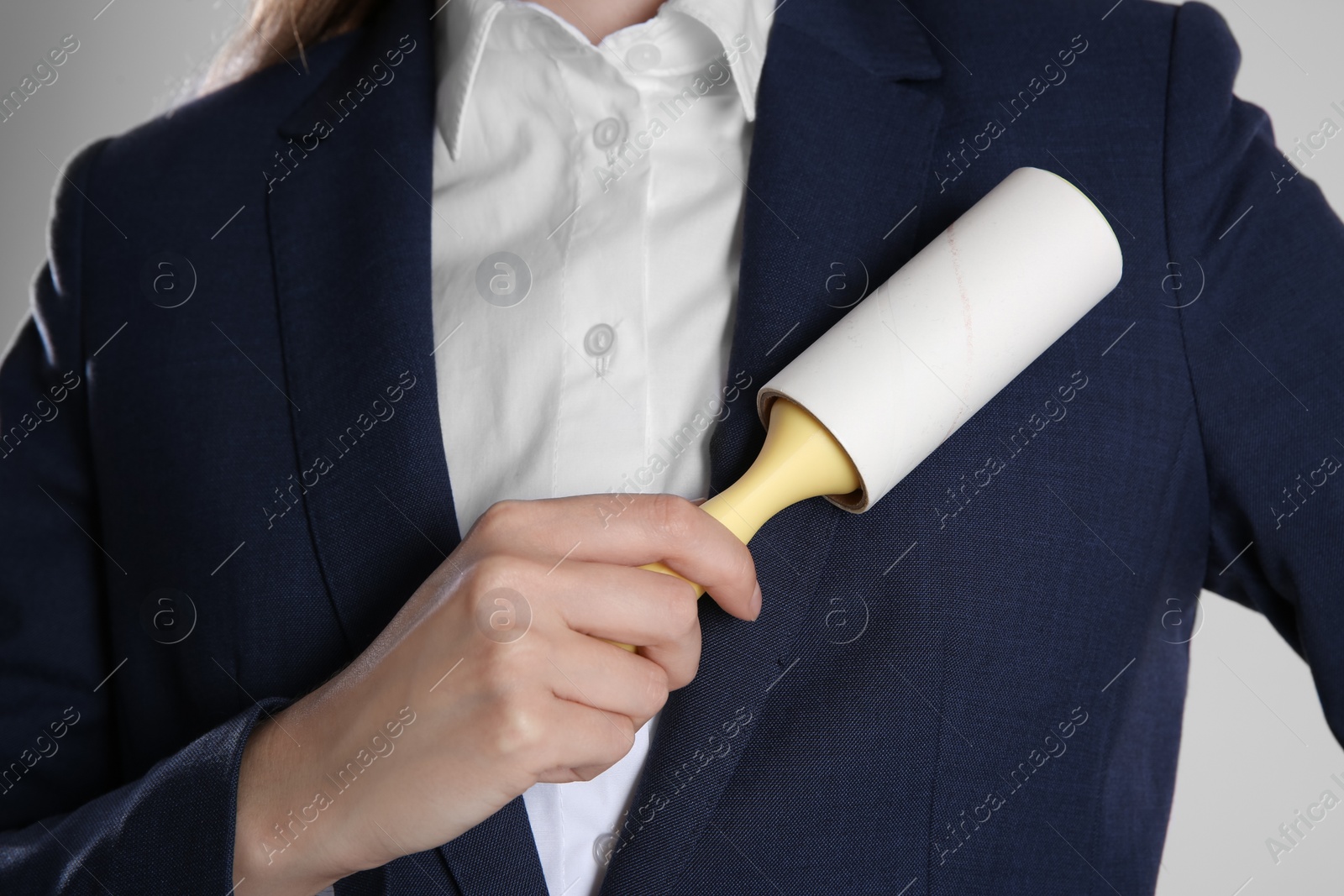 Photo of Woman cleaning dark blue jacket with lint roller on grey background, closeup