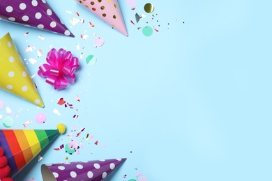 Photo of Flat lay composition with party hats, pink bow and confetti on light blue background, space for text. Birthday decor