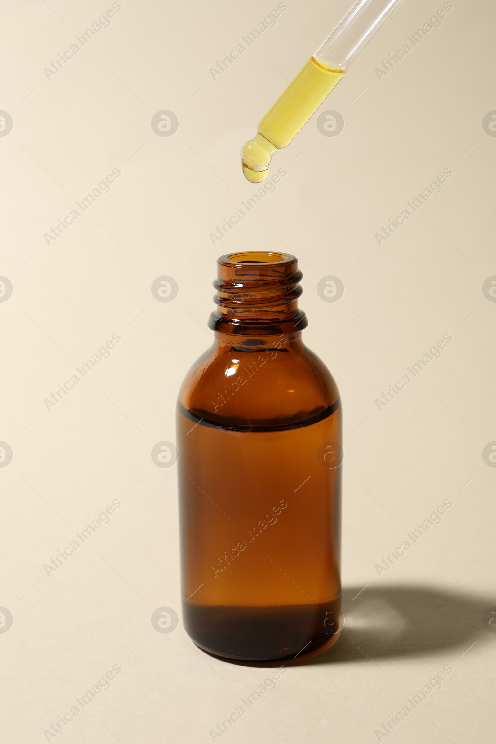 Photo of Dripping cosmetic oil from pipette into bottle on beige background
