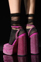 Woman wearing pink high heeled shoes with platform and square toes on black background, closeup