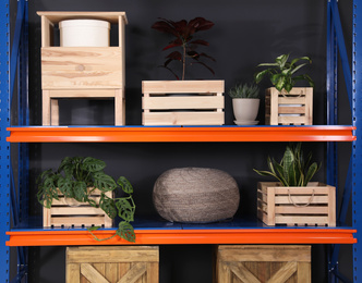 Photo of Metal shelving unit with wooden crates and different household stuff near black wall indoors