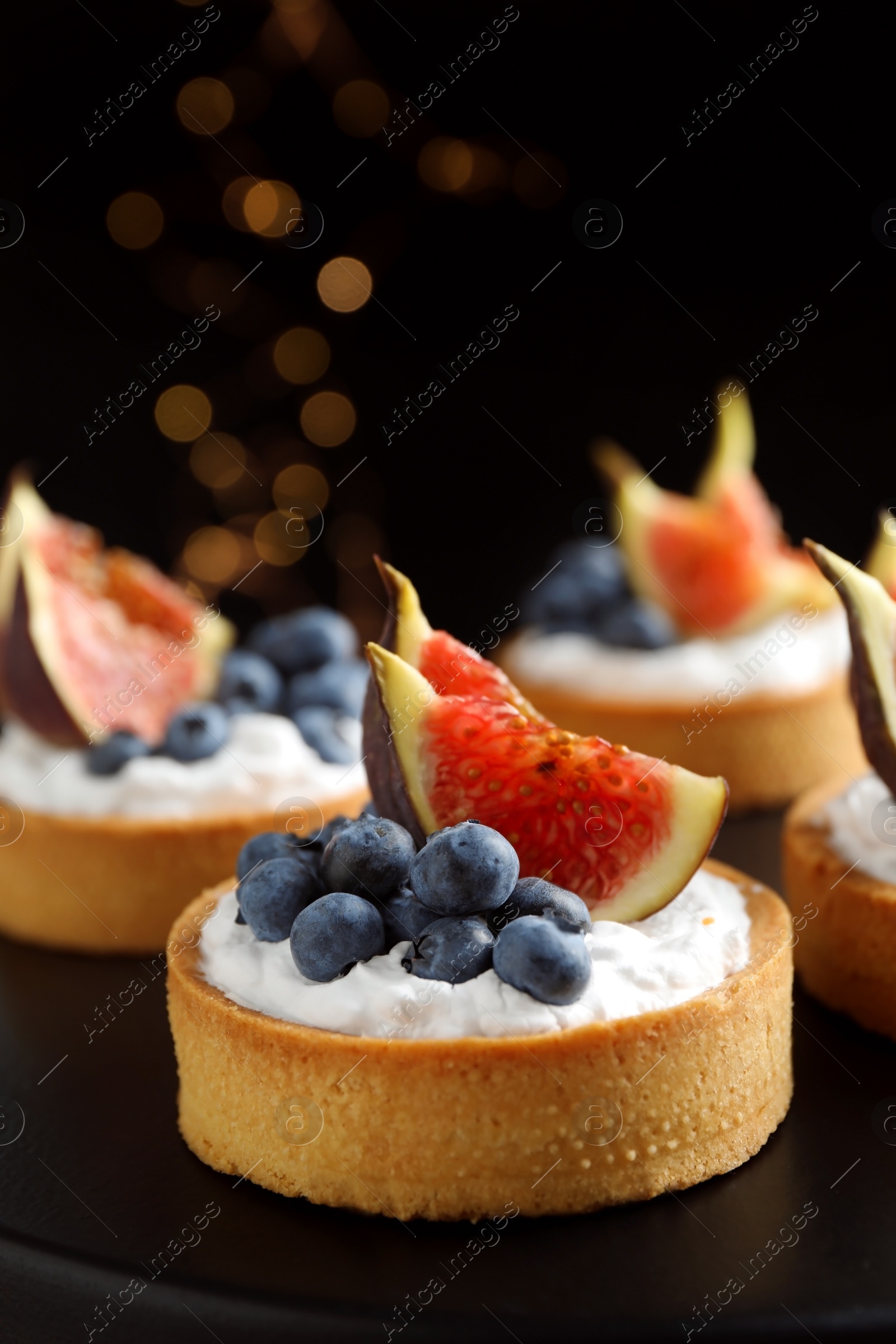 Photo of Tarts with blueberries and figs on black table against dark background, closeup. Delicious pastries