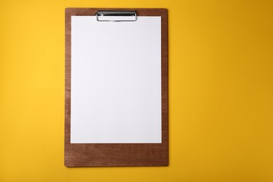 Photo of Wooden clipboard with sheet of blank paper on yellow background, top view. Space for text