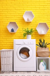 Photo of Laundry room interior with modern washing machine near yellow brick wall