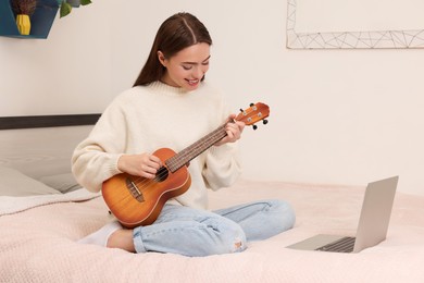 Photo of Happy young woman learning to play ukulele with online music course via laptop at home. Time for hobby