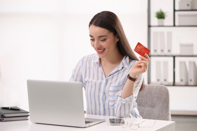 Woman with credit card using laptop for online shopping at white table indoors