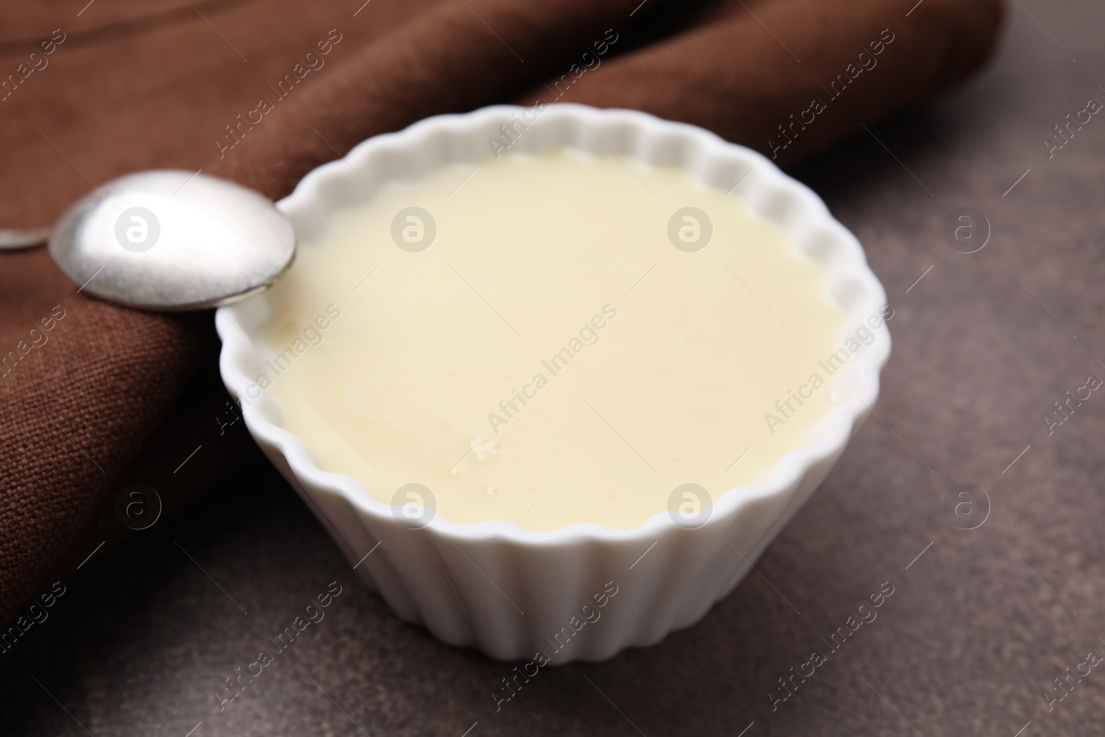 Bowl with condensed milk and spoon on brown table, closeup Photo of Bowl with condensed milk and spoon on brown table, closeup