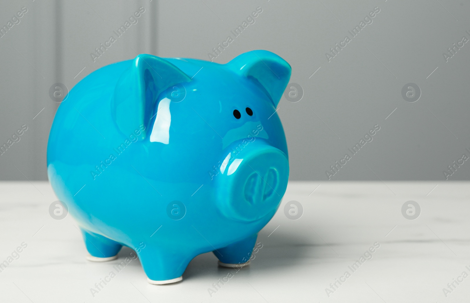 Photo of Ceramic piggy bank on white marble table. Space for text