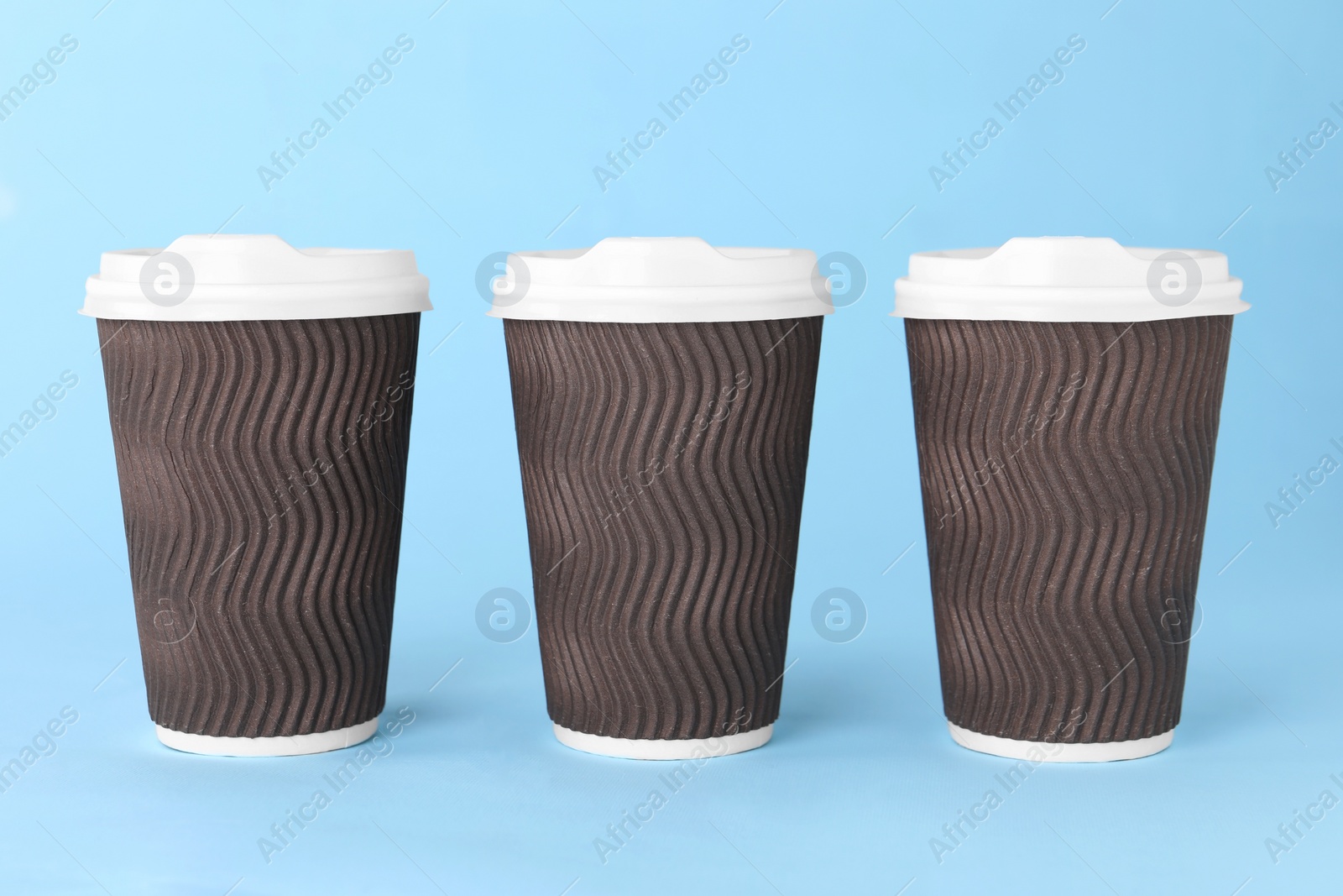 Photo of Paper cups with white lids on light blue background. Coffee to go