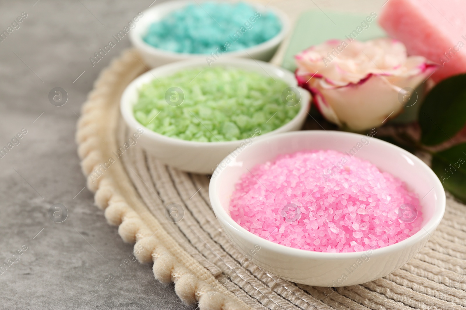 Photo of Different types of aromatic sea salt and beautiful flower on grey textured table, closeup. Space for text