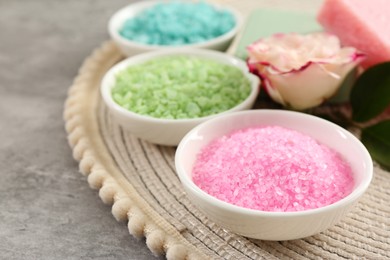 Different types of aromatic sea salt and beautiful flower on grey textured table, closeup. Space for text