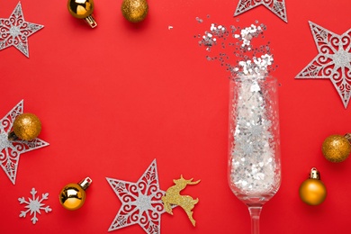 Photo of Flat lay composition with shiny confetti spilled out of champagne glass near Christmas decorations on red background, space for text