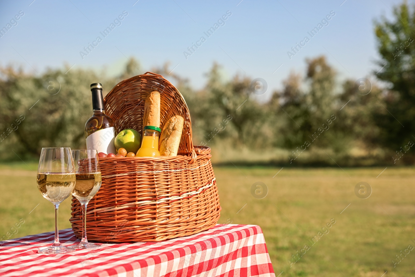 Photo of Wicker picnic basket with wine and snacks on table in park. Space for text